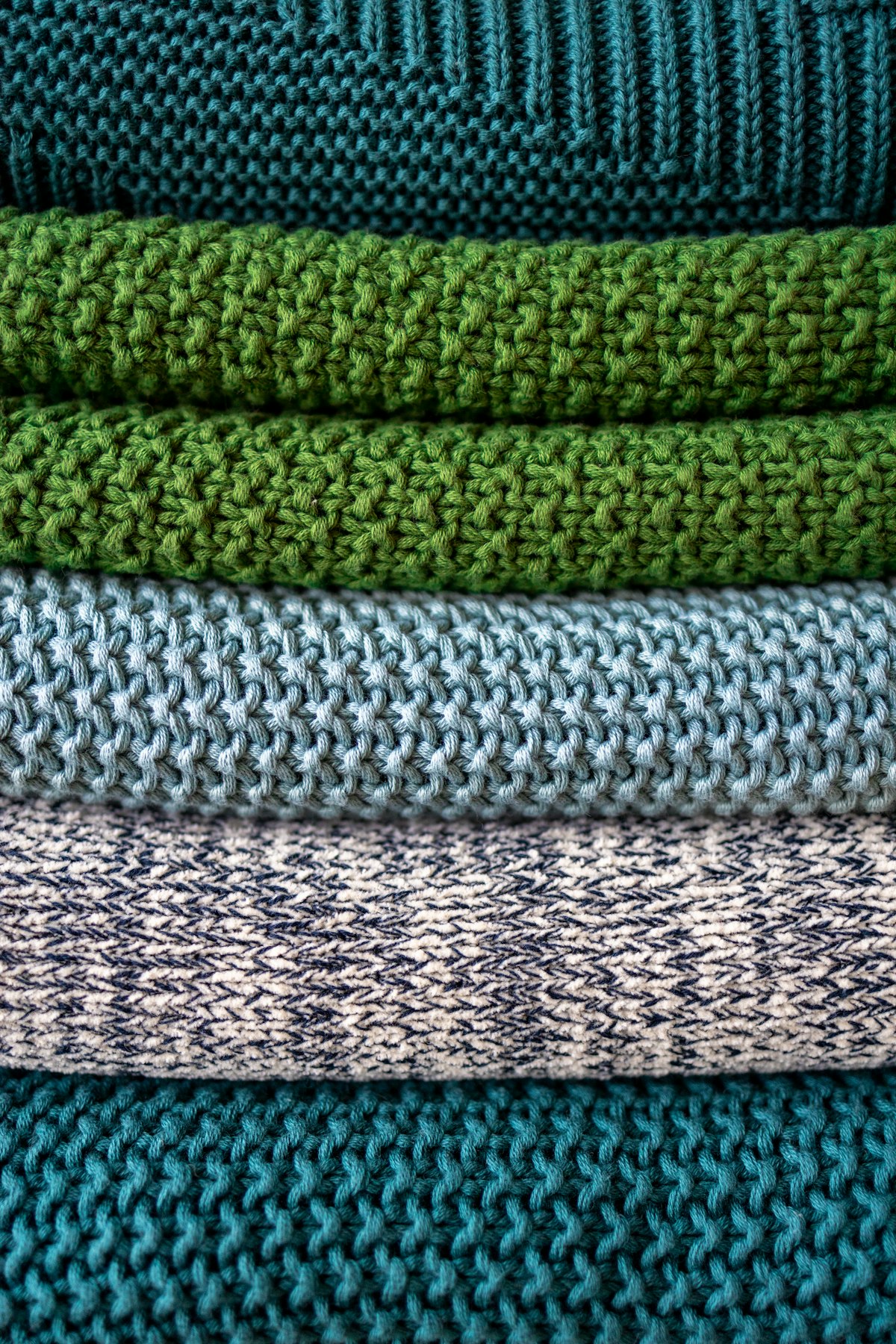 Tricôs dobrados em tons de verde, azul e cru empilhados